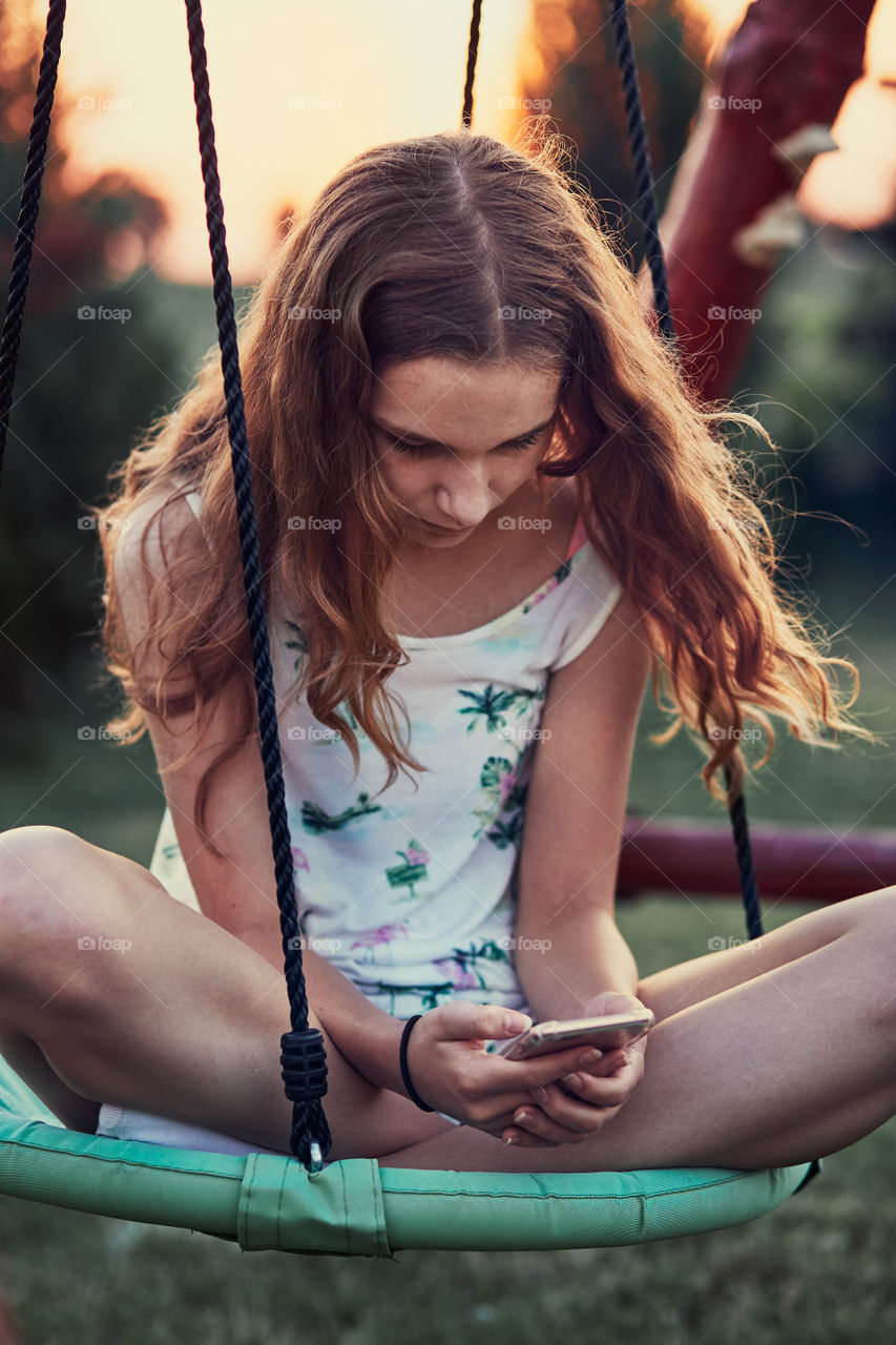 Young woman using mobile phone smartphone sitting on swing in a backyard. Candid people, real moments, authentic situations