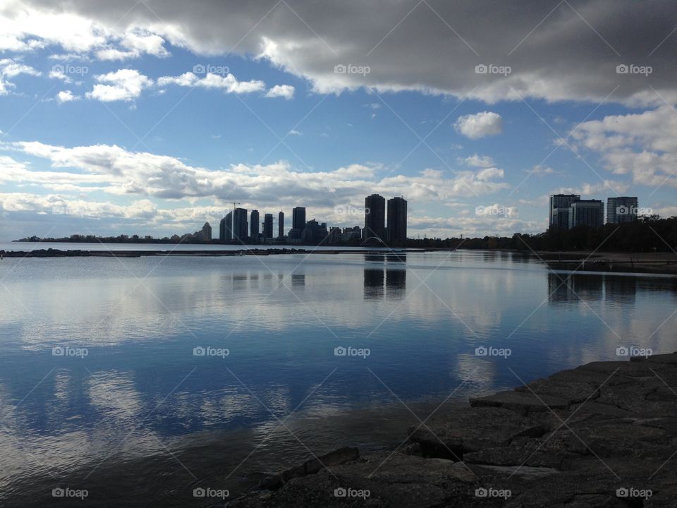 Toronto skyline. The water so calm there's a perfect reflection. Beautiful blue sky with fluffy white clouds. Perfection and calm for such a busy bustling city. 
