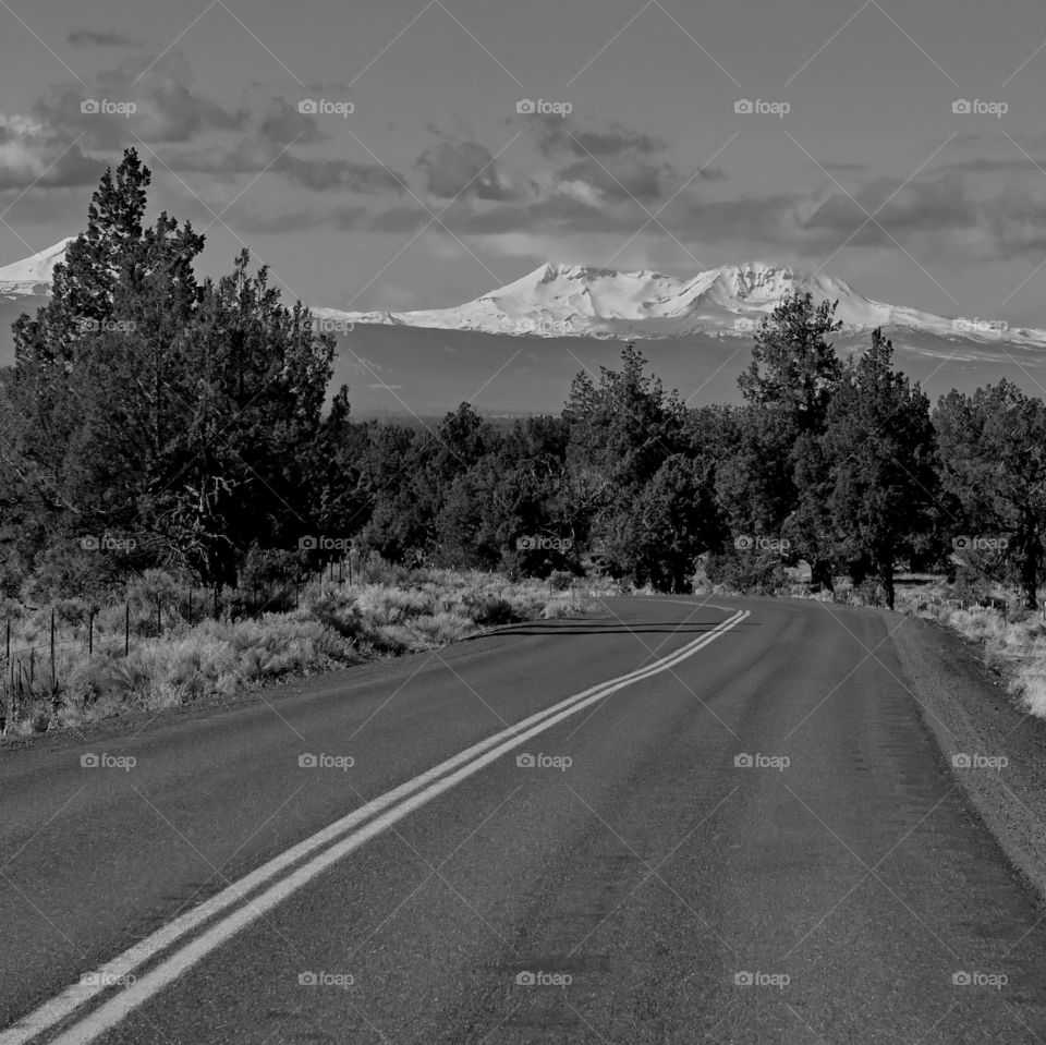 A back country road leads the eye through the forest to the snow covered Three Sisters in Oregon's Cascade Mountains. 