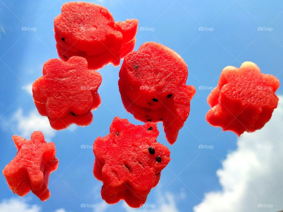 Summer meal.  Pieces of red ripe watermelon of various shapes lie on a mirror surface.  A blue sky with white clouds reflects on a mirror surface