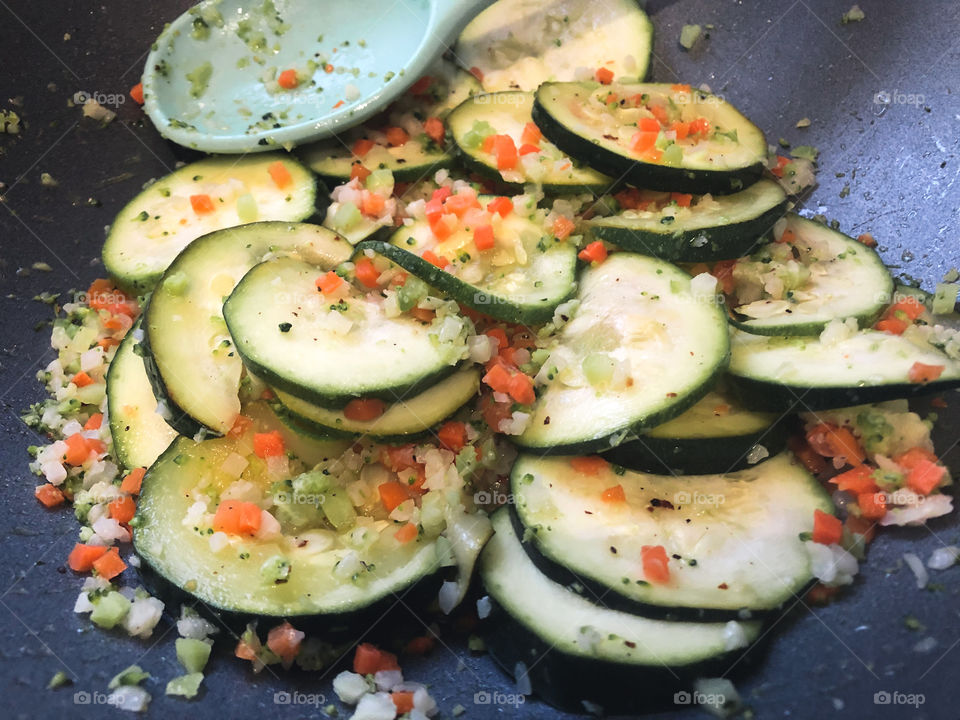 Homegrown courgettes with other diced vegetables in a wok with a blue spoon