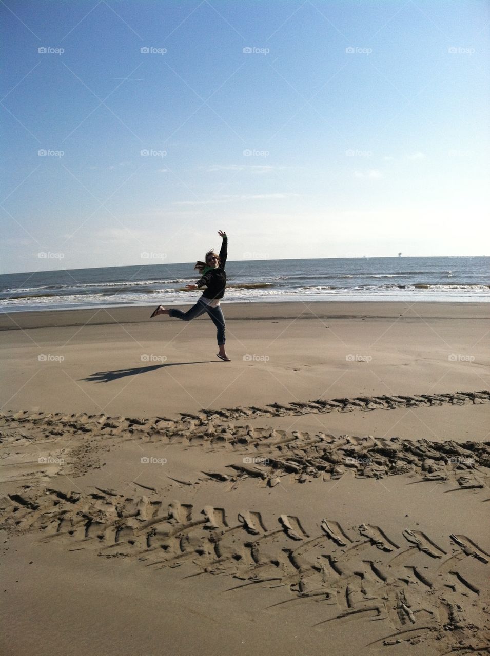 Woman jumping on the beach with tire tracks in the sand