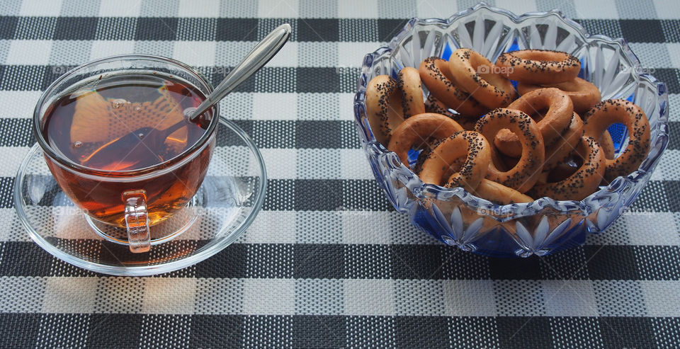 Tea in a cup and bagels with poppy seeds in a vase.