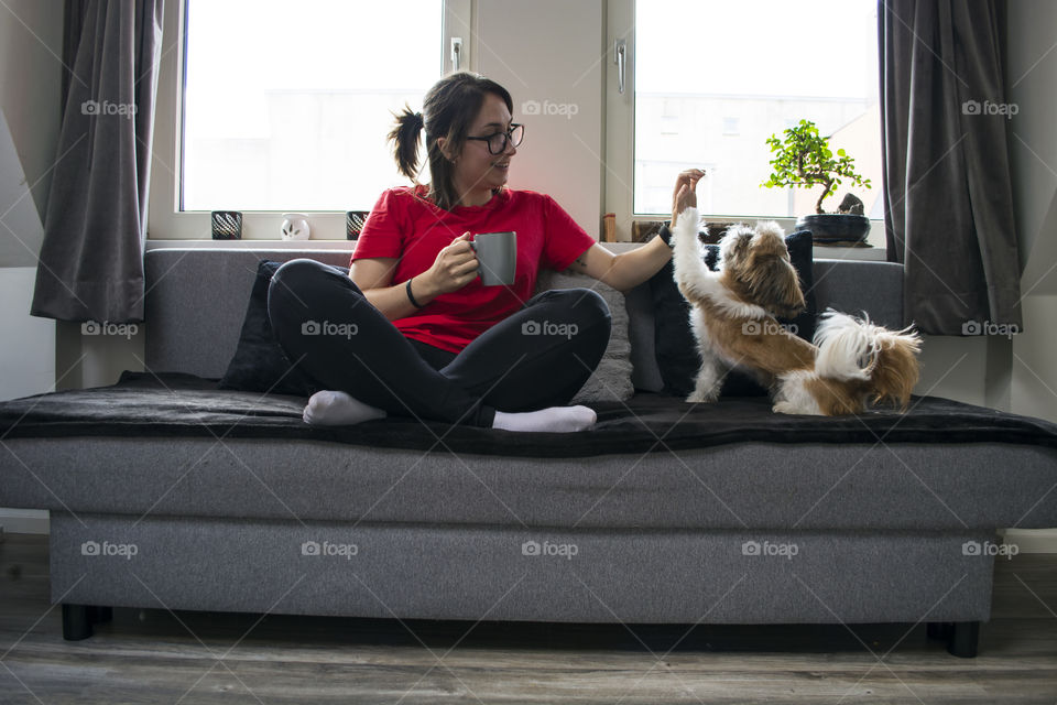 Girl drinking coffee and playing with her dog on the couch