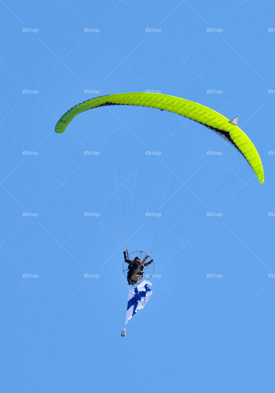 Helsinki, Finland - 9 June 2017: Unidentified pilot performing aerobatics stunts with a paramotor and a Finnish flag in the  Kaivopuisto Air Show 2017 on sunny summer evening in Helsinki, Finland. 