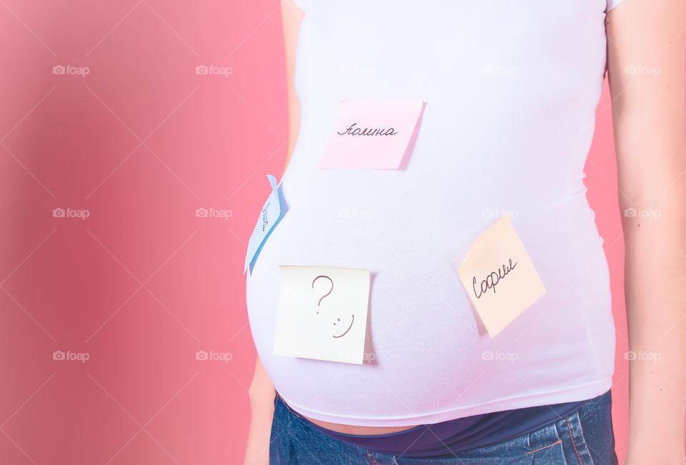 Baby names of female baby. Cropped image of pregnant woman with baby names of belly standing on pink background