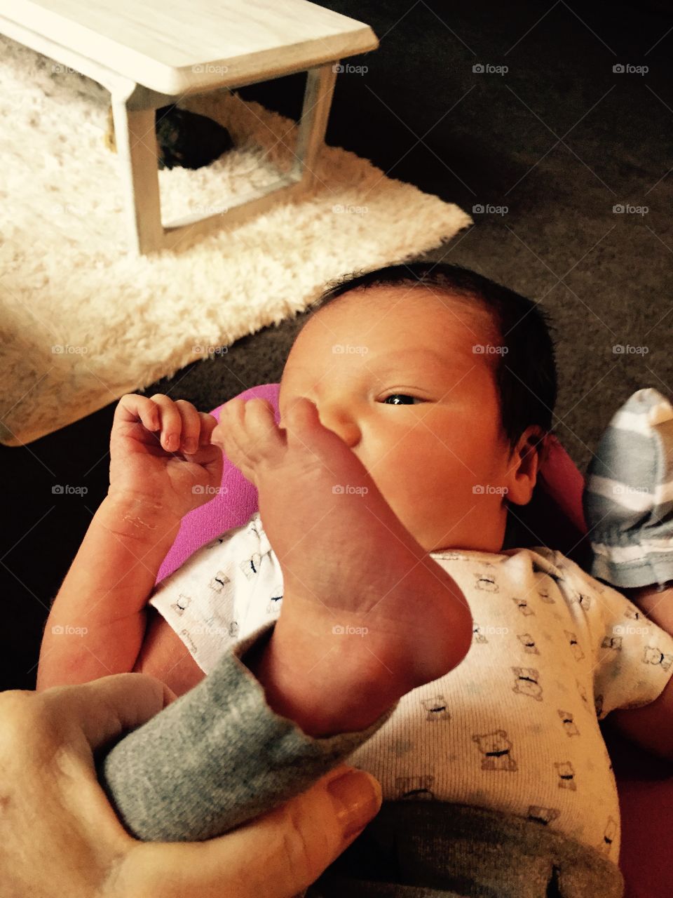 One week old newborn  baby boy with foot up in the air coveting part of view of his sweet face, hand in the air.