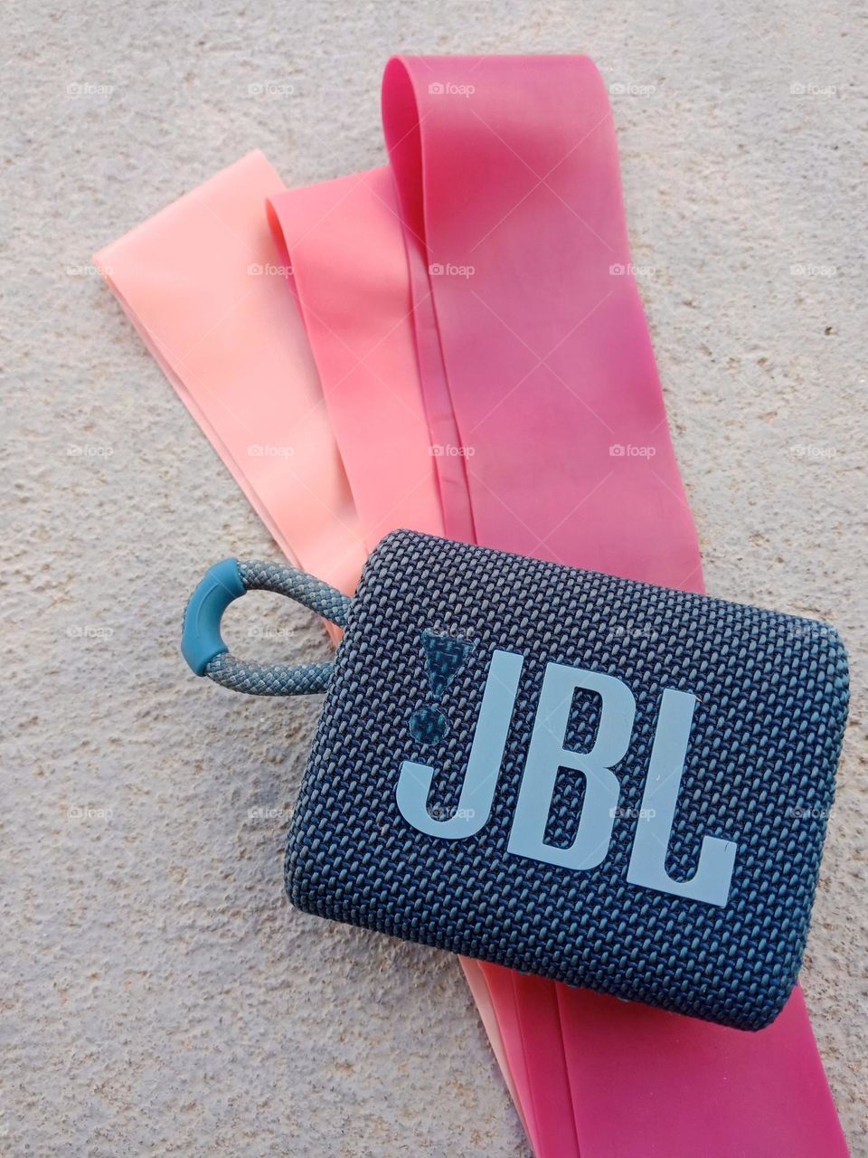 Blue JBL go box,  pink exercise bands,  grey floor