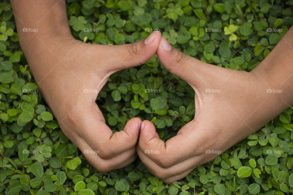 Little boys hand forming a heart "I love you"on grass background.