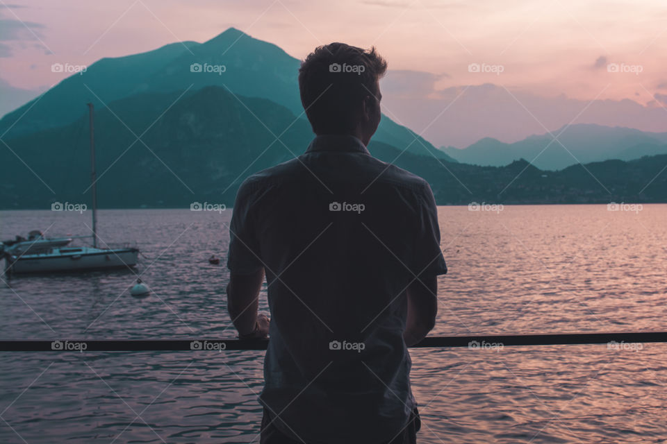 A man looking out to mountains and a lake during sunset 