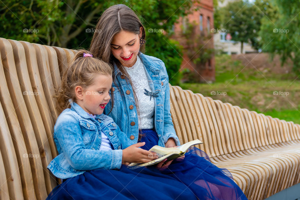 Two sisters sit on a bench in the park and reading book