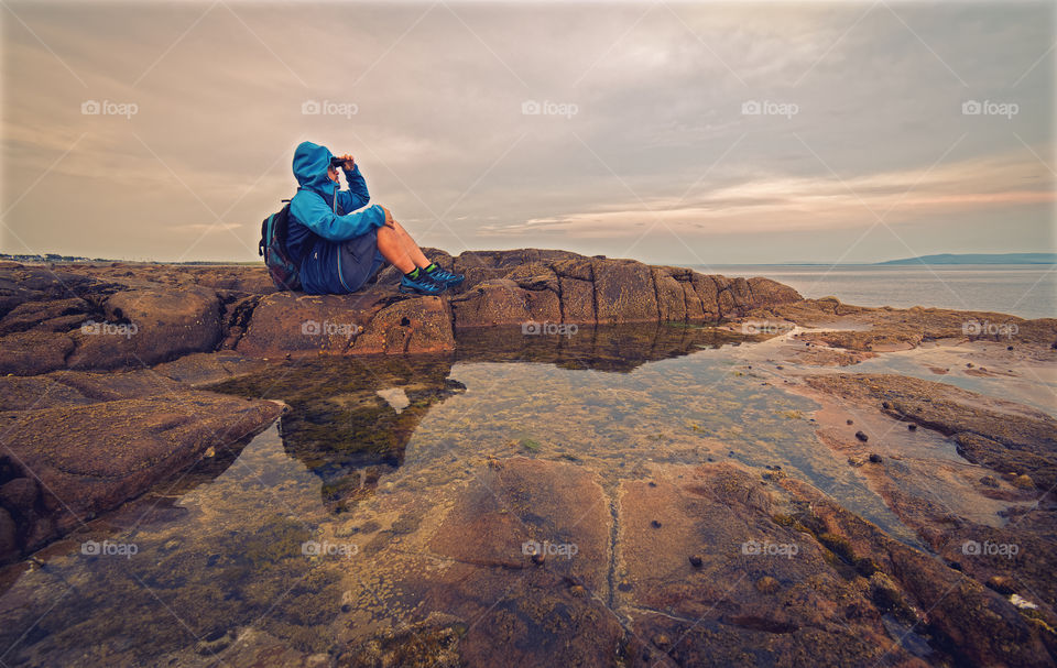 Man sitting on the rock reflected in the water at Barna, Galway, Ireland