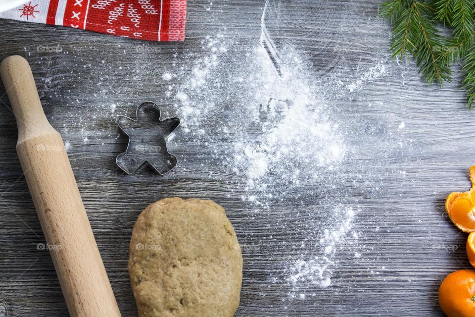 Christmas, gingerbread cookies on a wooden table sprinkled with flour, with tangerines and a green Christmas tree.