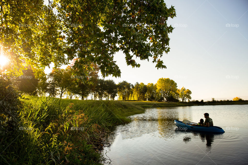 Summer is a time of outdoor activities and having fun in water. Dad and his girl rowing on a kayak on a lake during sunset. Summer reminds me of family time and being together.