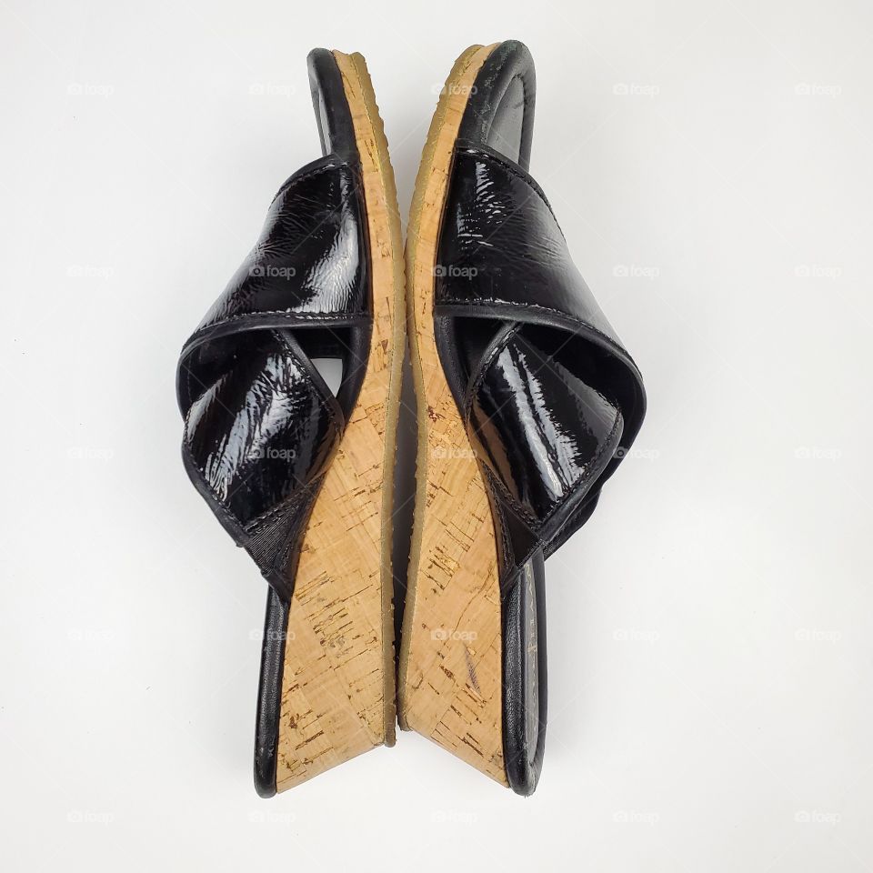 side view of patent black leather shoes with cork soles on a white background