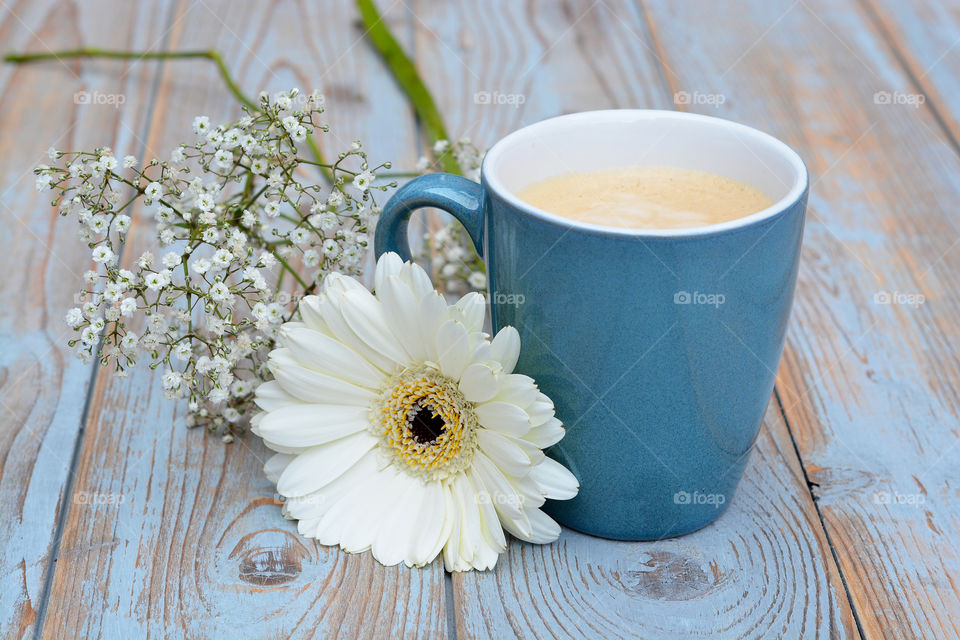 blue cup of coffee on a wooden table background with white gerber daisy