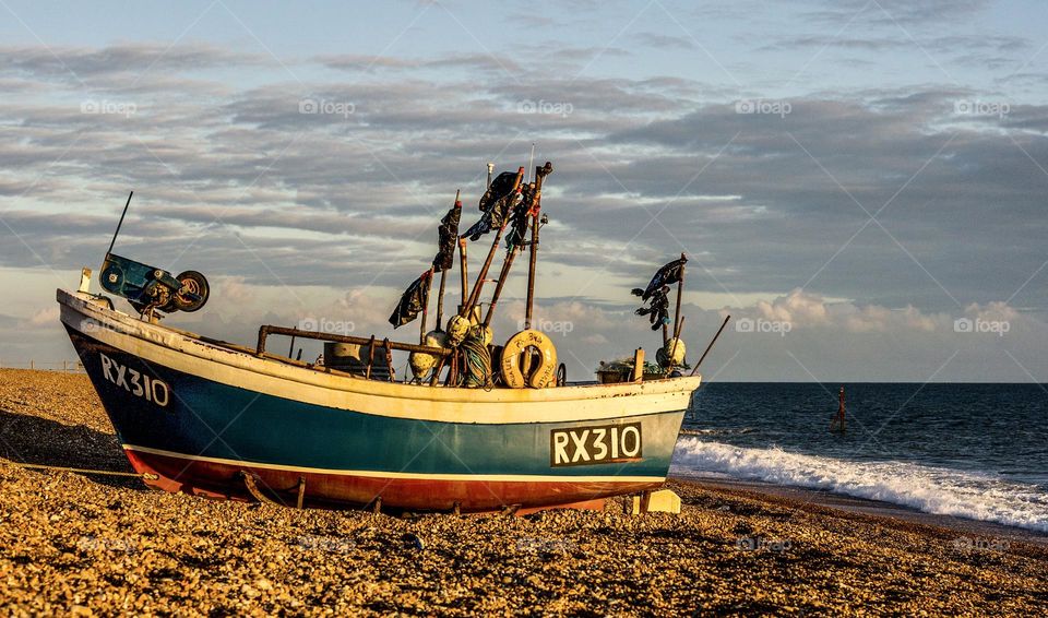 A boat sits on the pebbled, working fishing beach in the late afternoon sun at Hastings, UK