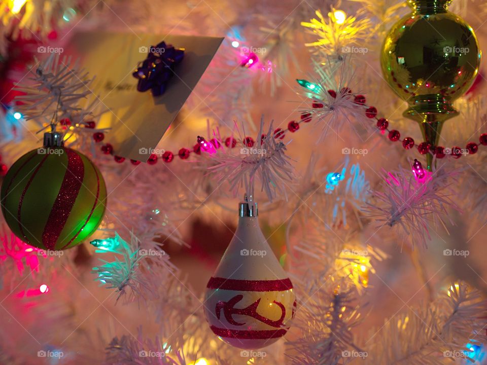 Ornaments in hanging on a white Christmas tree bathed in beautiful soft colored lights during the holiday season. 