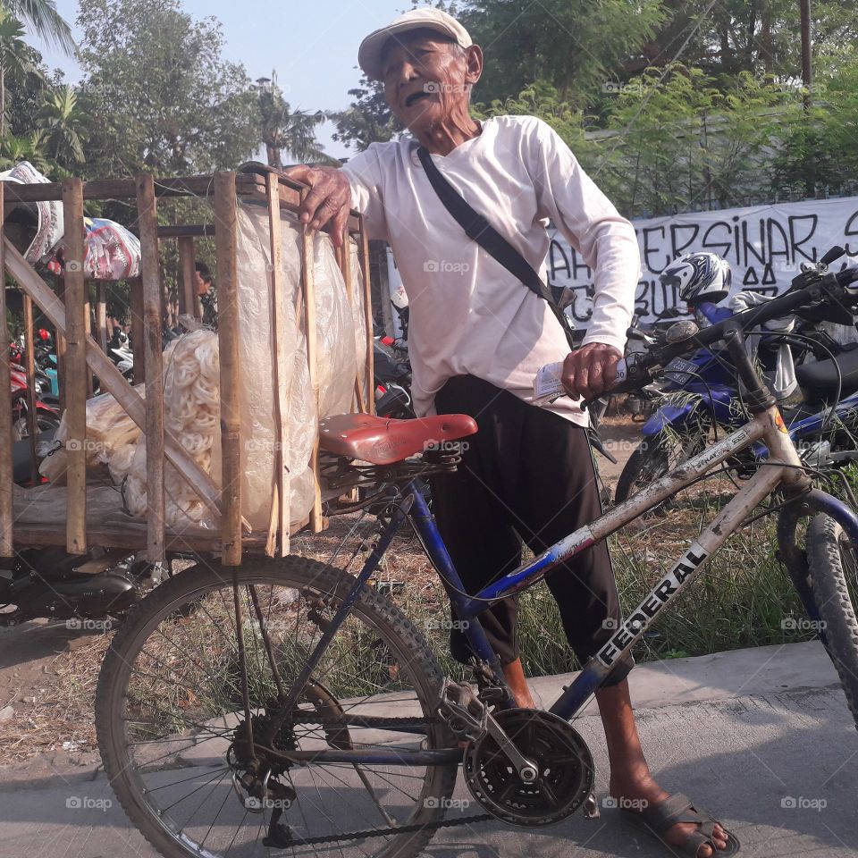 An old man is enjoying his work.  He sells crackers by riding a bicycle in Semarang, Indonesia. Photo taken on October 13, 2019.