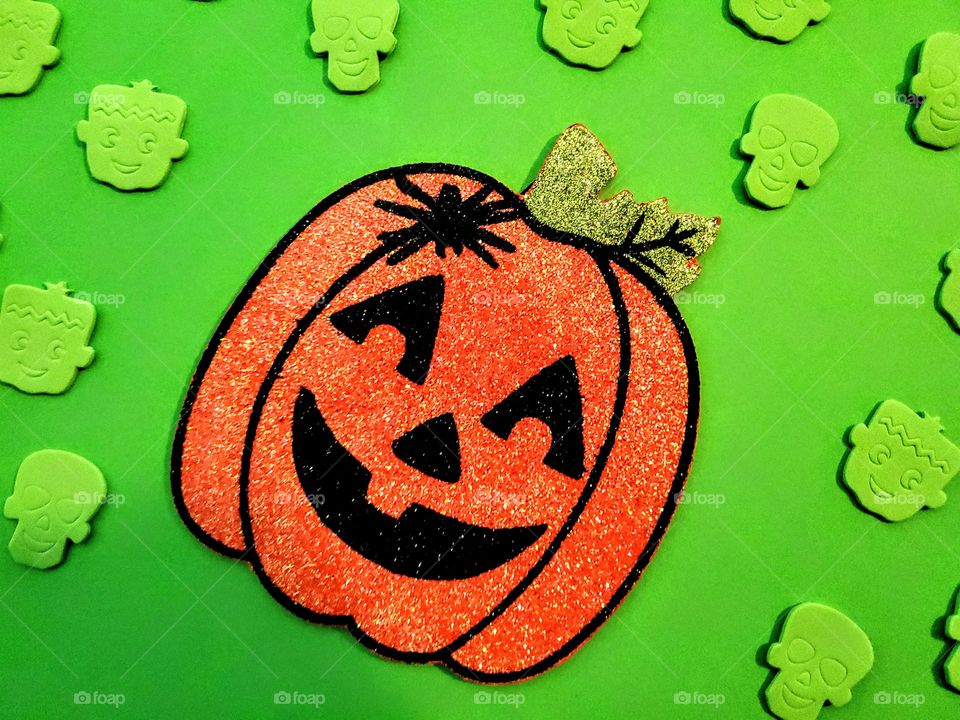 Colorful bright neon green Halloween flat lay with a glitter bright orange flat Happy face pumpkin