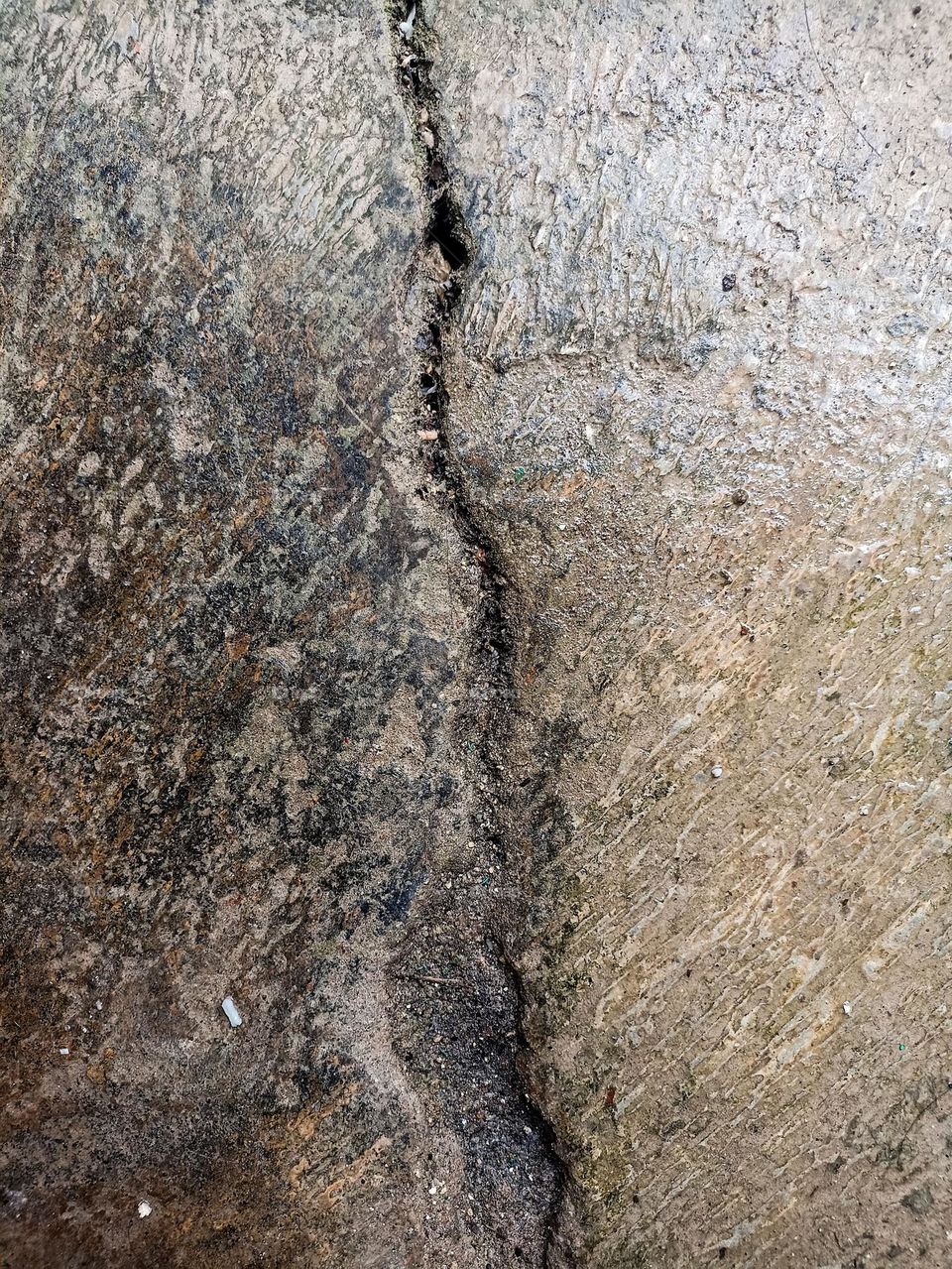 Close-up view of a large crack on a rough, dusty concrete surface. The concrete surface looks rough, with dust and dirt stuck around it