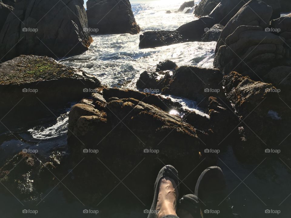A man and a woman’s feet on a rock at the ocean shore