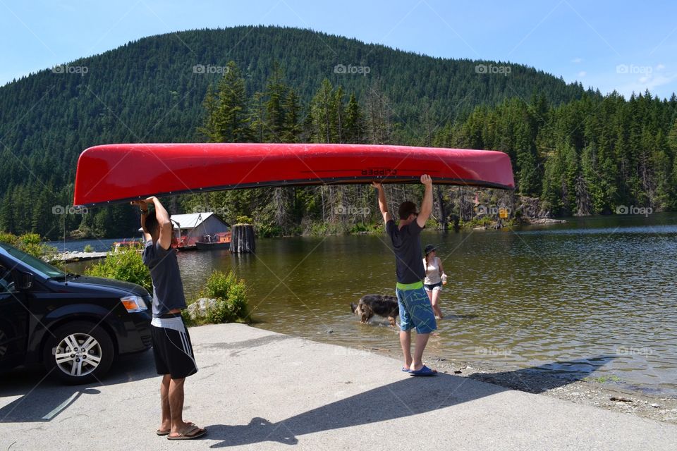 Carrying the kayak to lake. Male youth carrying a red kayak to lake