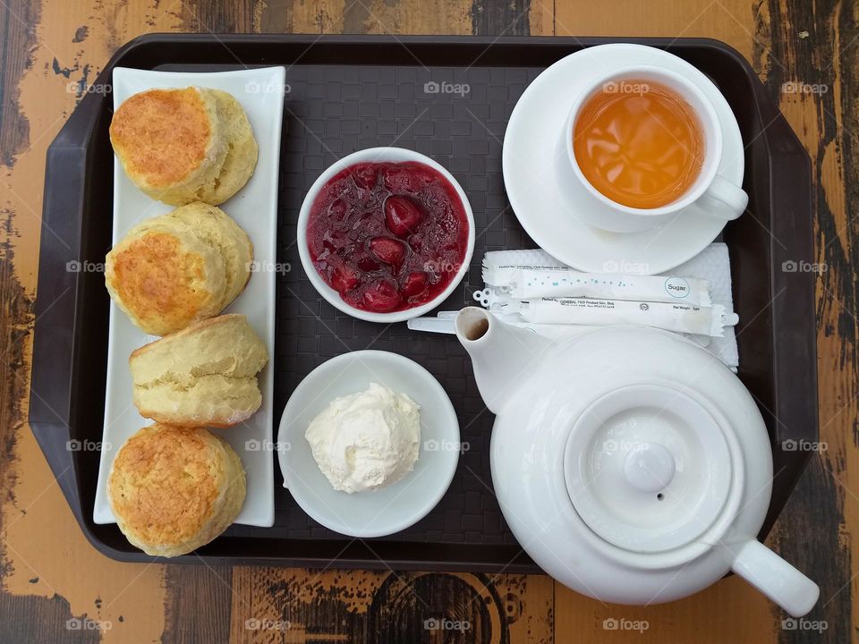A set of scones with cream and strawberry jam. Also hot tea on the table.