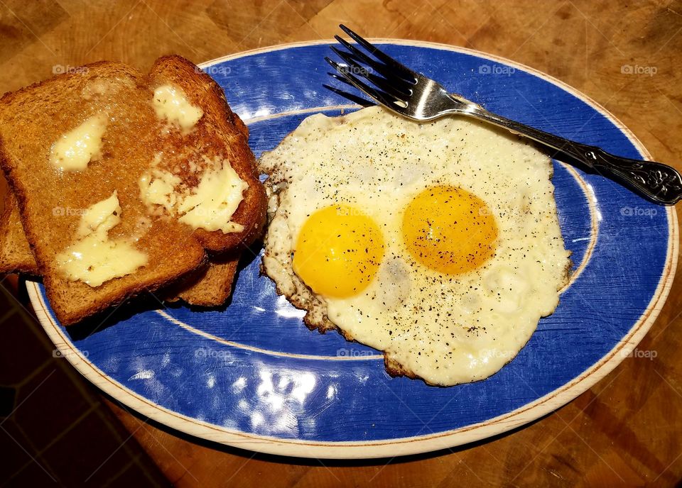 Breakfast toast, butter, sunny side up eggs, fork, on a blue plate!