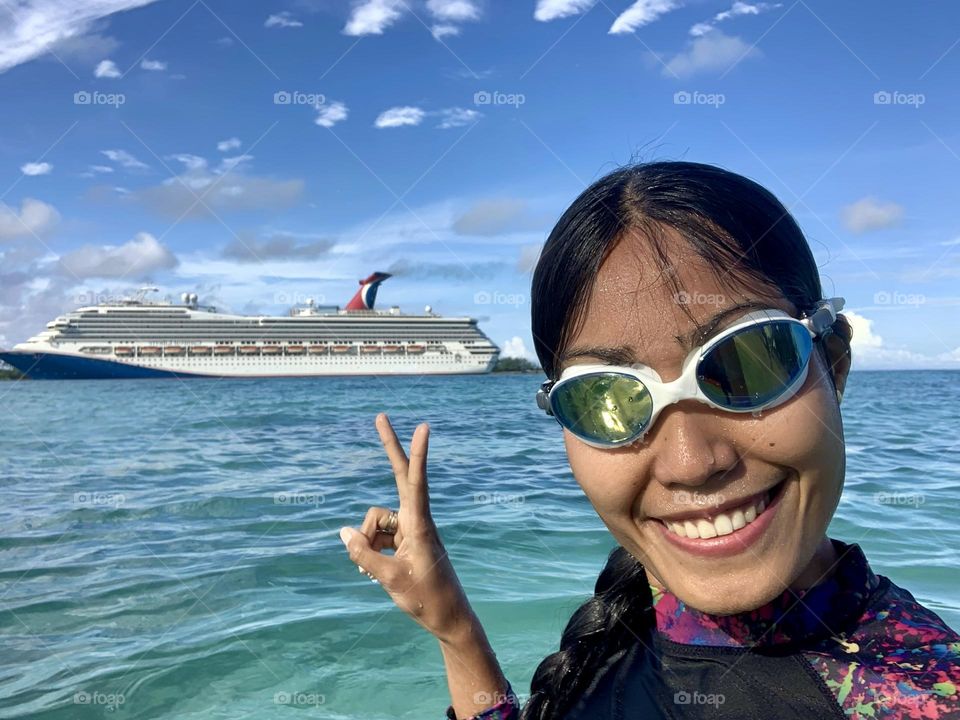 Selfie of young adult woman wearing goggles with smile on her face and make a sign of peace I front of the cruise ship. 