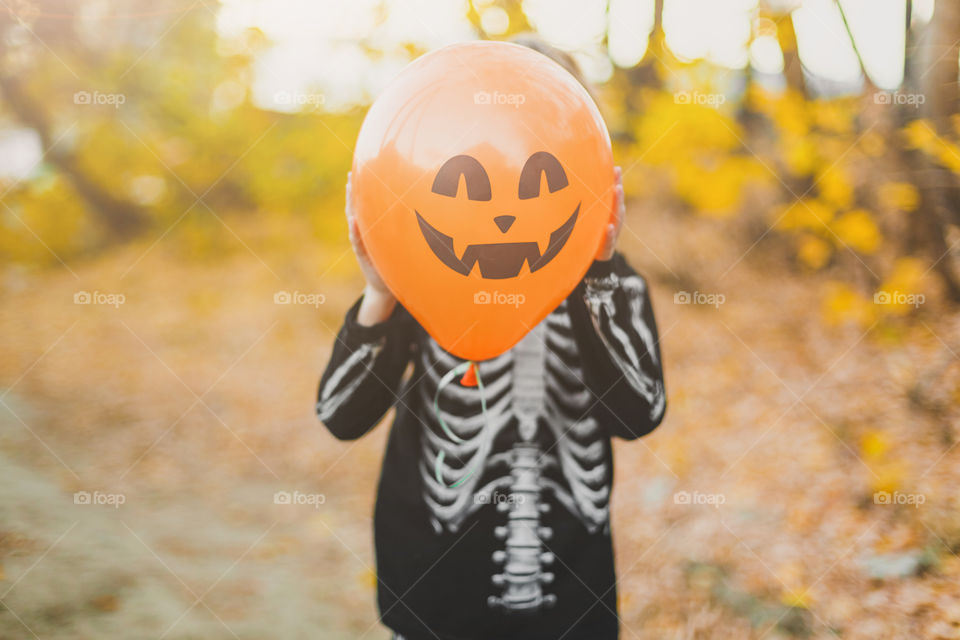 A boy in a skeleton costume holds an orange balloon with a face. Making faces, fooling around.