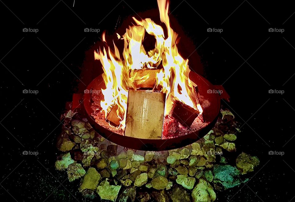 Dancing flames emerge from a circular fireplace surrounded by multi-colored stones. This picture was taken in 2019. Hypnotic Productions