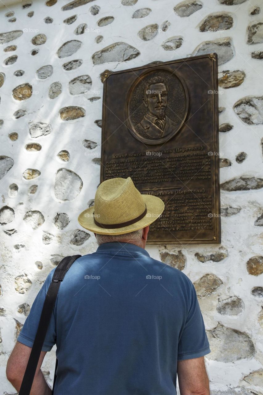 Back view of a man with a hat looks at a memorial plaque