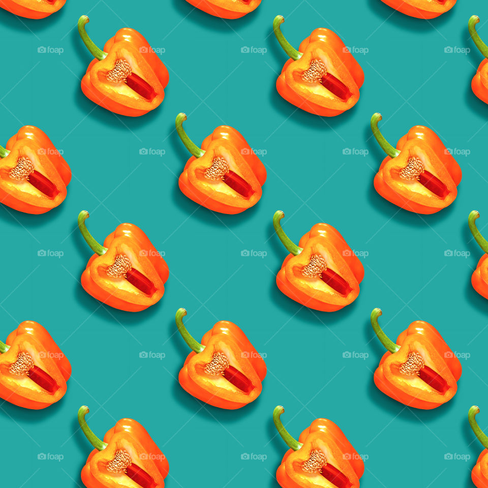 Repeating pattern of cut orange sweet bell peppers with green ponytails. The concept of healthy, ecological food. Beautiful contrasting ornament of fresh juicy pepper on a blue background