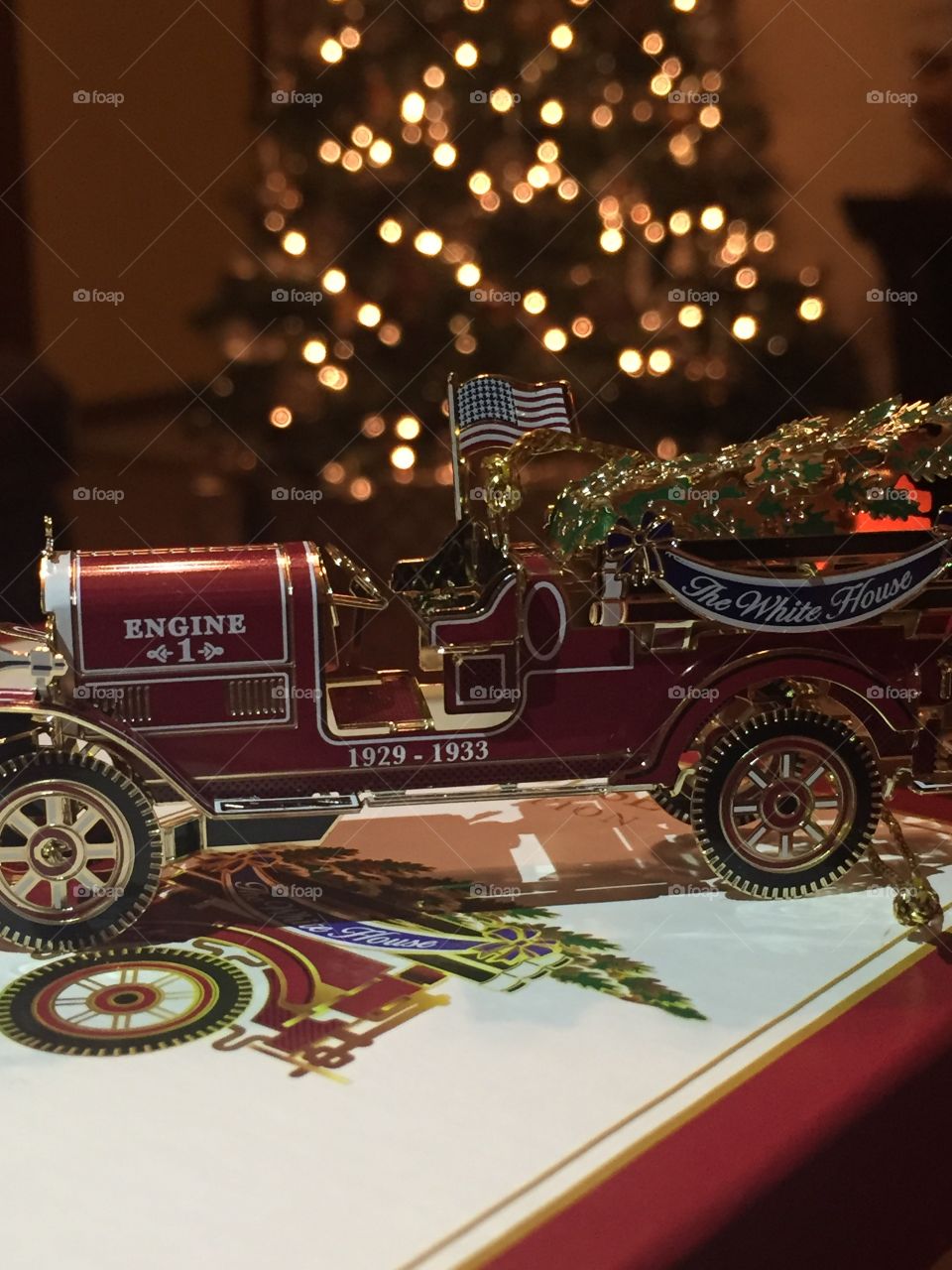 Fire truck ornament with glowing Christmas tree lights in the background. 