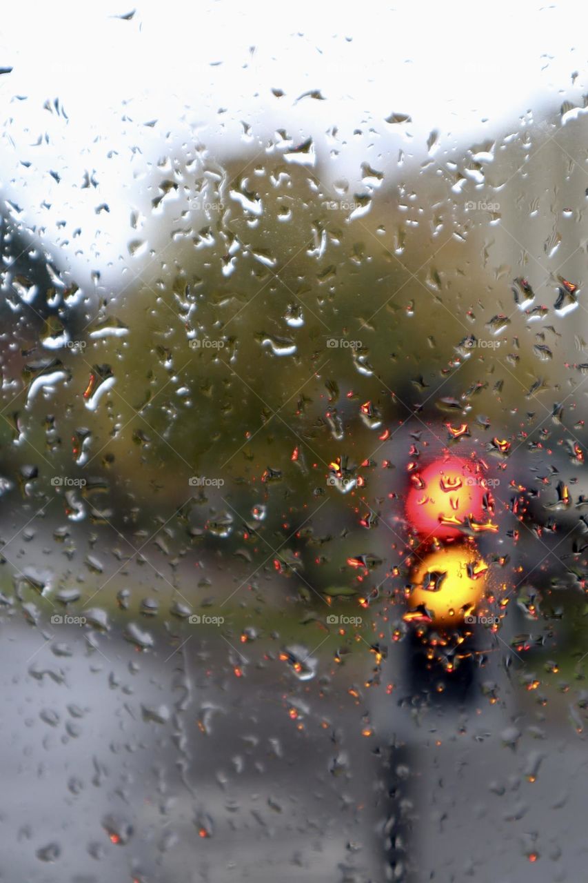 Red and yellow traffic light behind window with rain drops 