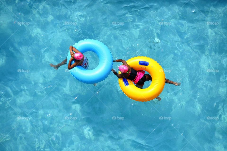 Two young girls enjoy splashing around in a swimming pool.