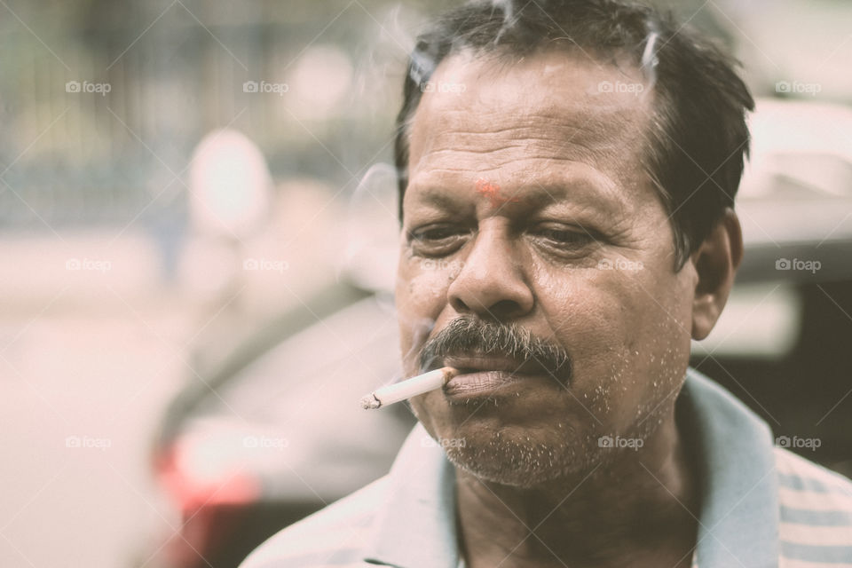 Portrait of a A mid adult senior mature man of Asian and Indian Ethnicity is smoking cigarette. Front View. Close up. Photography taken on 31 May 2019 on World No Tobacco or anti Tobacco Day, in a city street of India, South Asia.