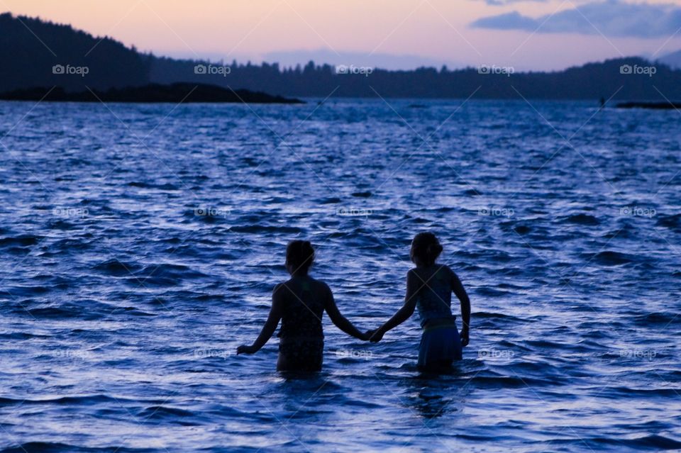 My 2 daughters, bravely inch hand-in-hand into the cold Pacific water to play in the last remnants of sunset. The black silhouettes of their bodies & the coastal tree line are a stark contrast against the inky blue water and the pink & purple sky. 👥