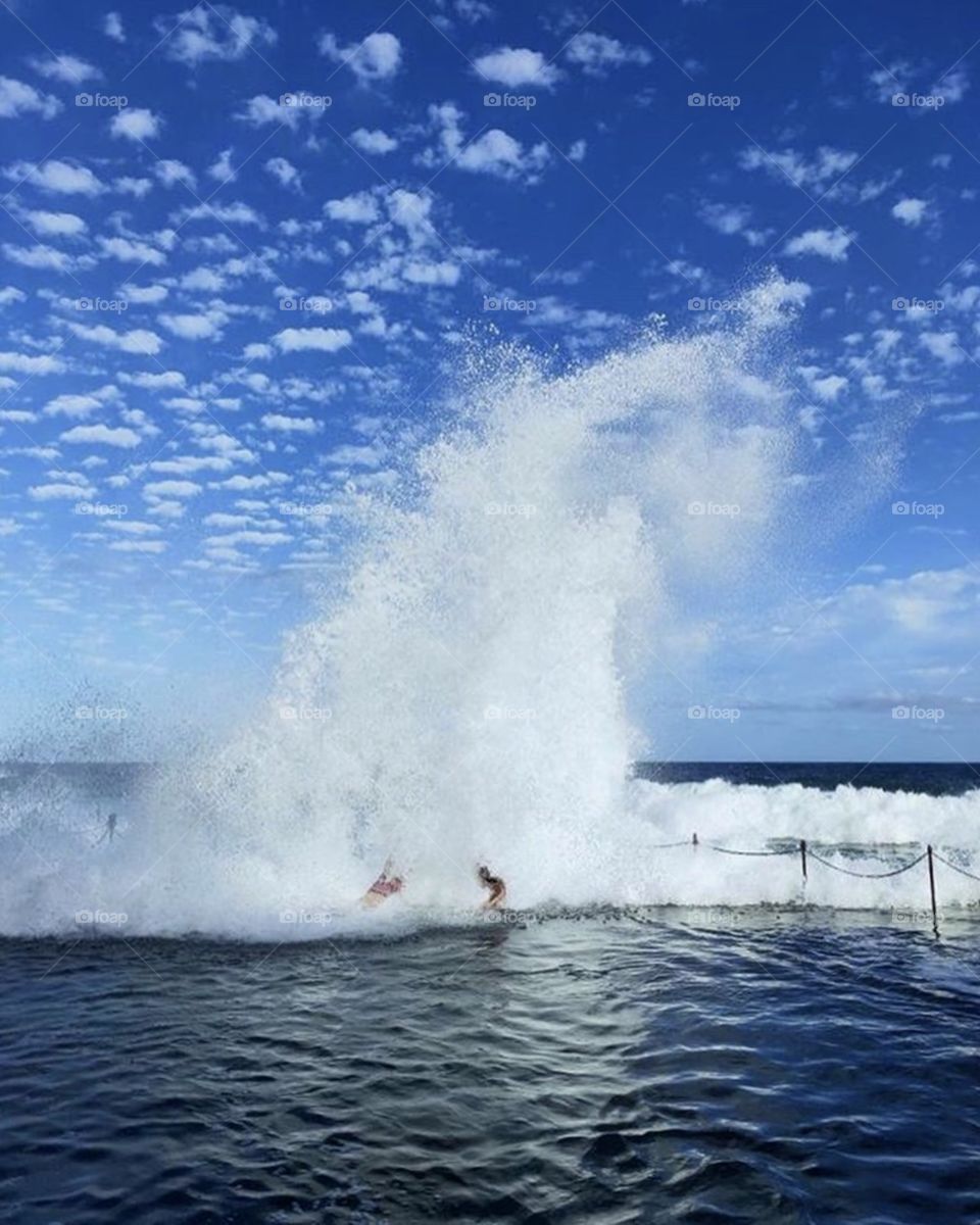 Large wave creating a massive splash as it pushes people into a rock pool on the Australian coast.