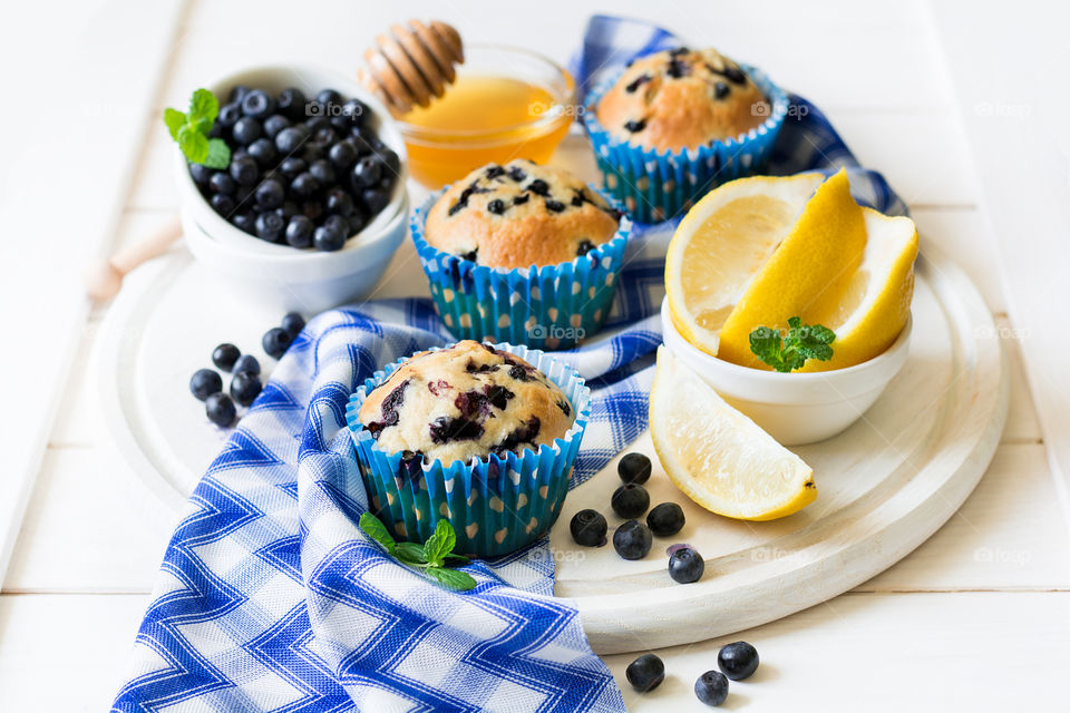 Blueberry muffins and berries with honey and lemon on white wooden background