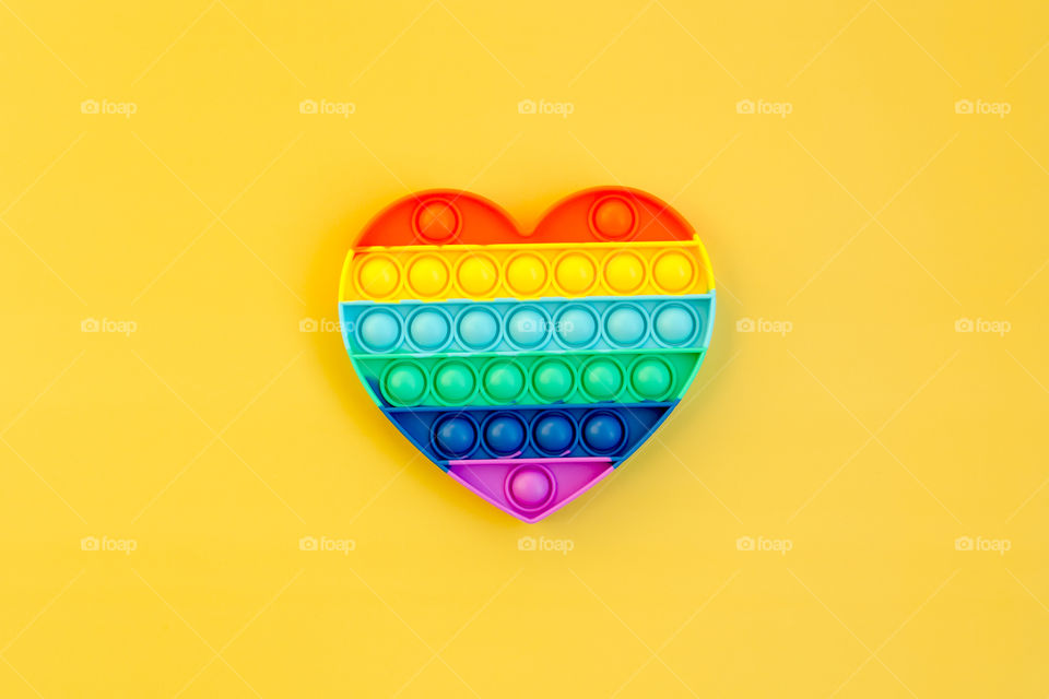 Top view of anti stress sensory toy Pop it rainbow heart on yellow background. Popular, trend toys in 2021