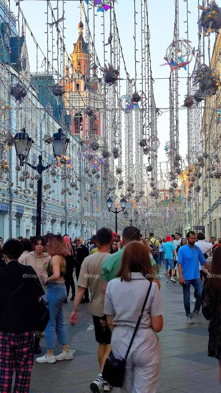 Summer in the city.  A crowd of people are walking down the street.  The bulk of the people are tourists who see the sights