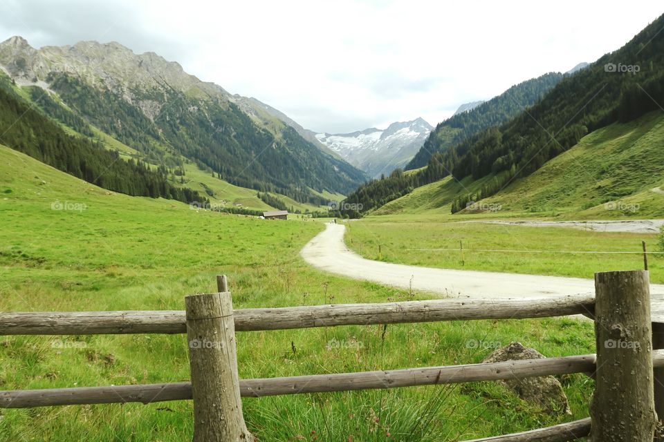 View into Zillertal valley in european alps (Austria, Tirol). Path leading along small stream through the valley.  Farm houses in background. summer time. Forest and high mountains surrounding in the rurial scene.