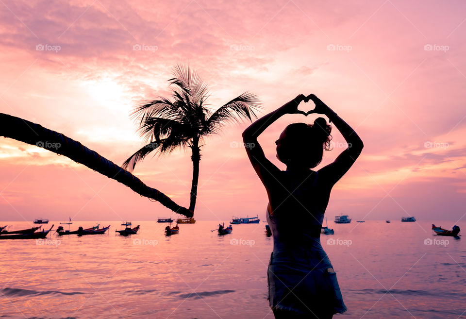 Woman making heart shape at beach at sunset