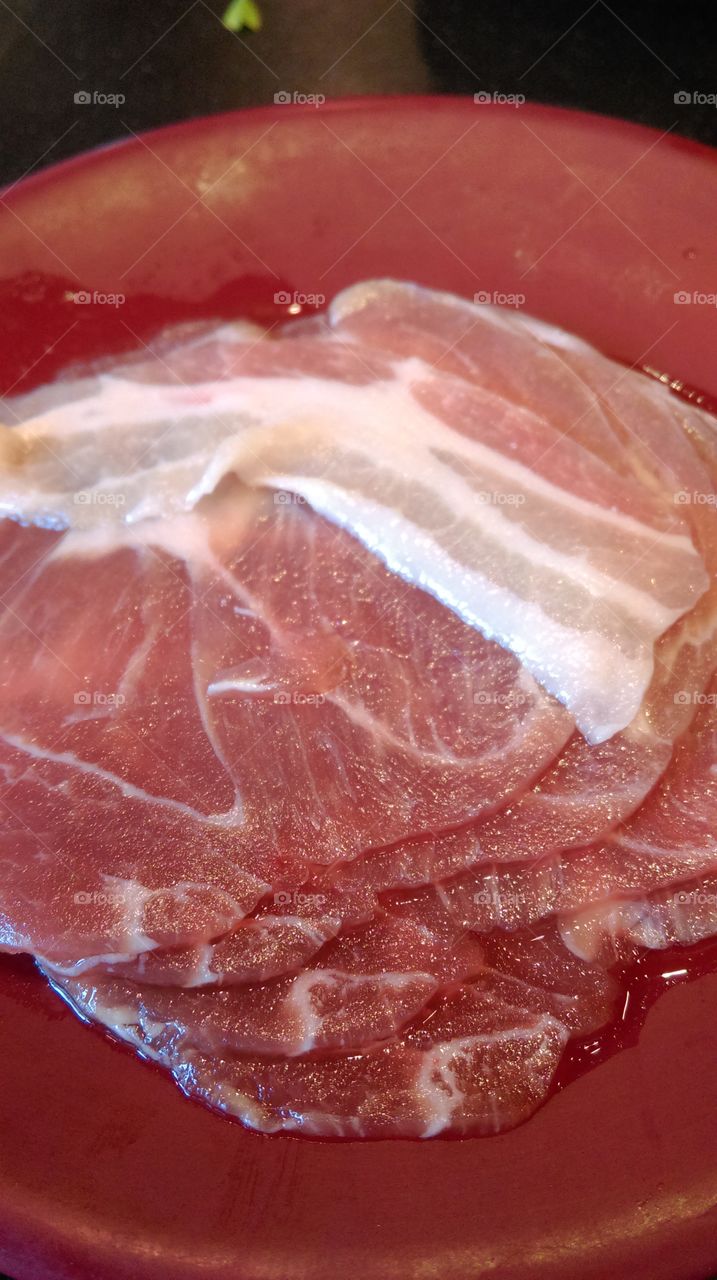 Raw slice pork on the red dish.