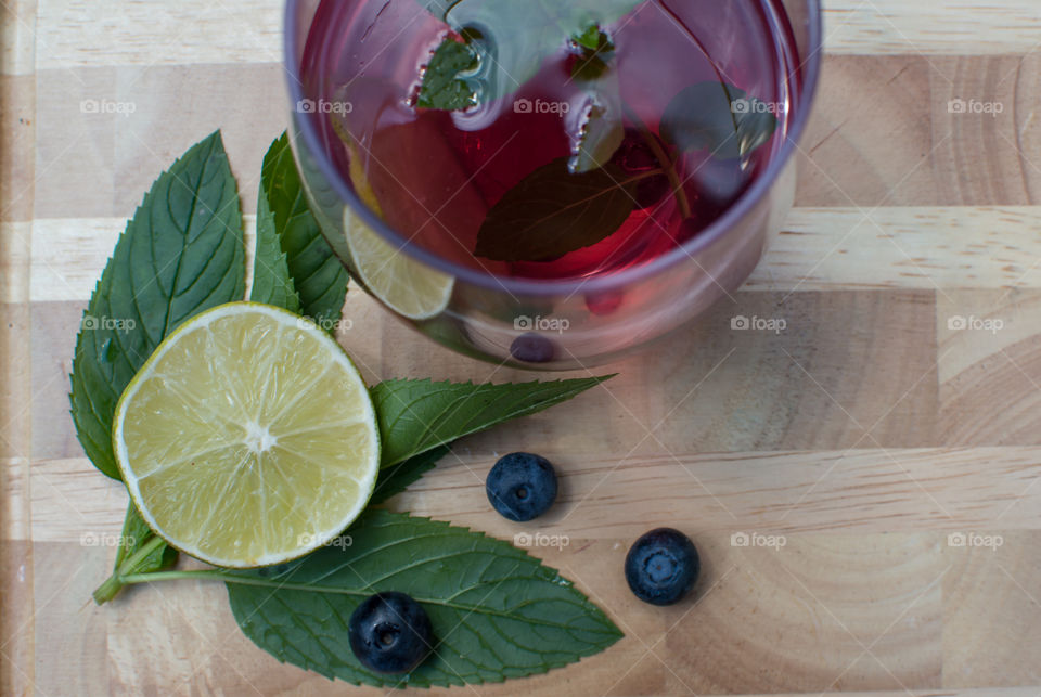 High angle view of blueberry lime and mint flavored water anyioxodant rich healthy homemade summer drink on wood table with fresh sliced lime, mint leaves and blueberry
