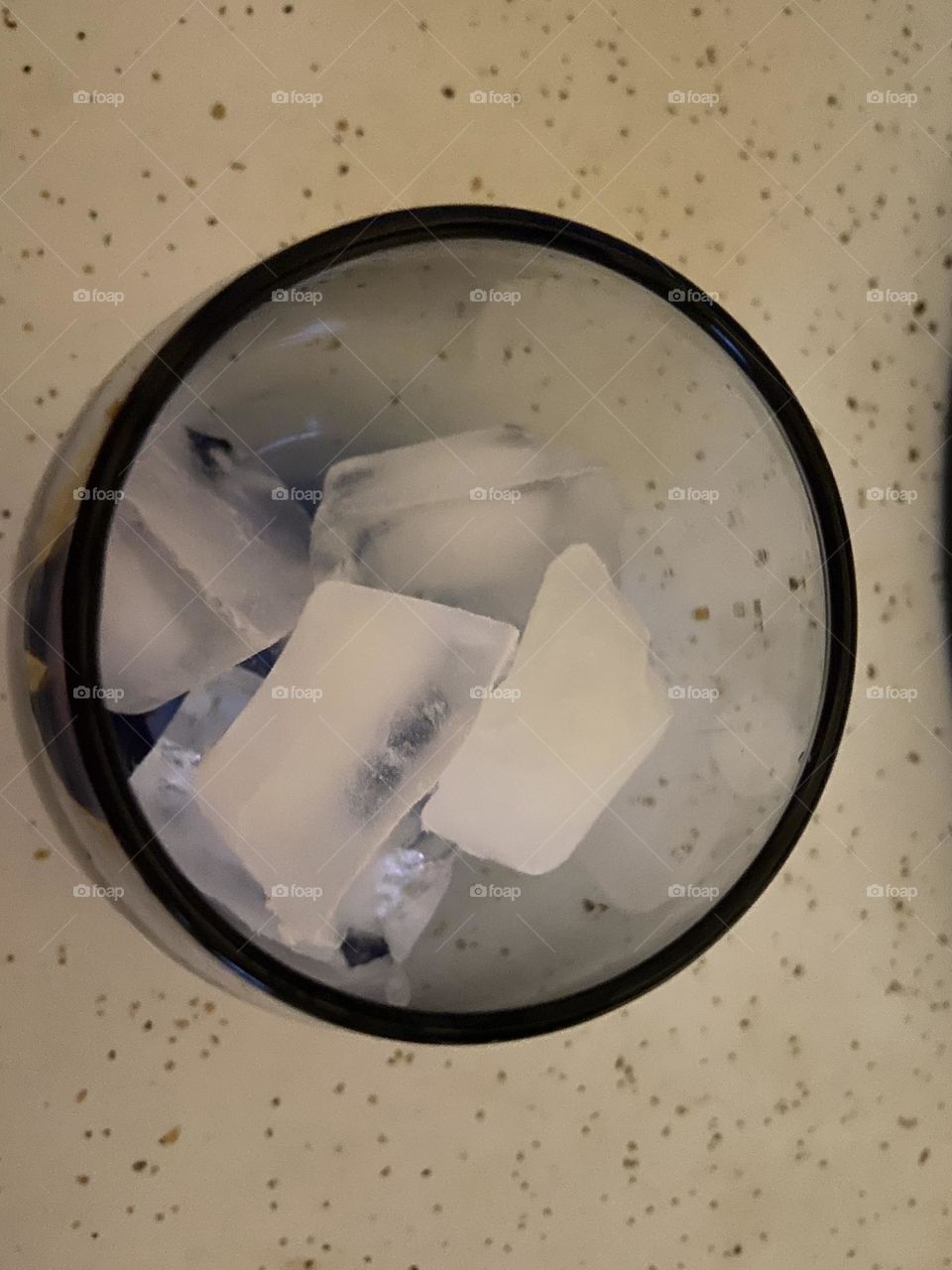 Ice cubes (aka frozen water) in a gray-tinted glass on the white speckled kitchen counter. 