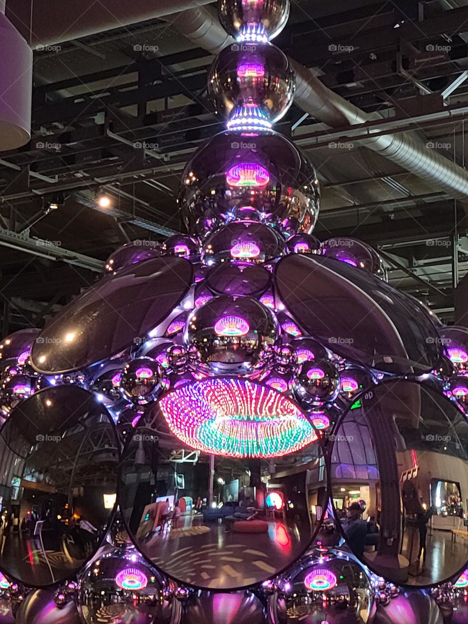 Hanging sculpture of mirror disks, almost like a disco ball, reflecting multiple colors, almost like eyes surrounding everything 