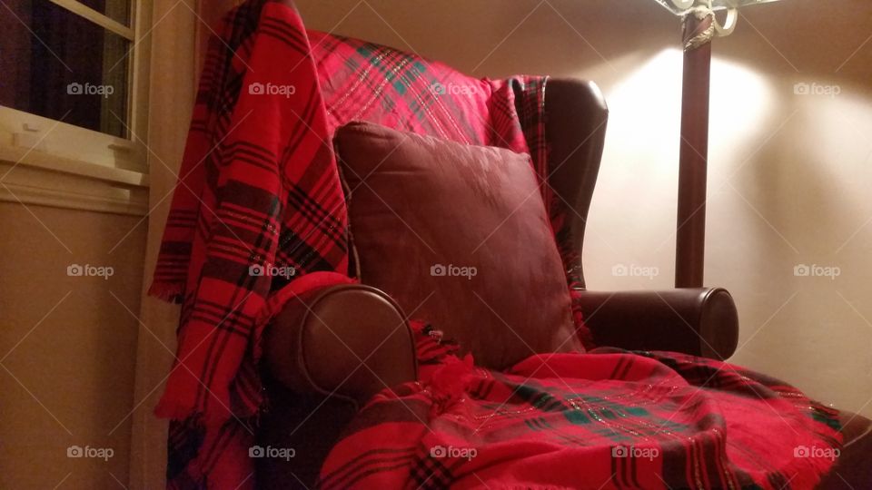 A chair with red plaid  covering by a window.